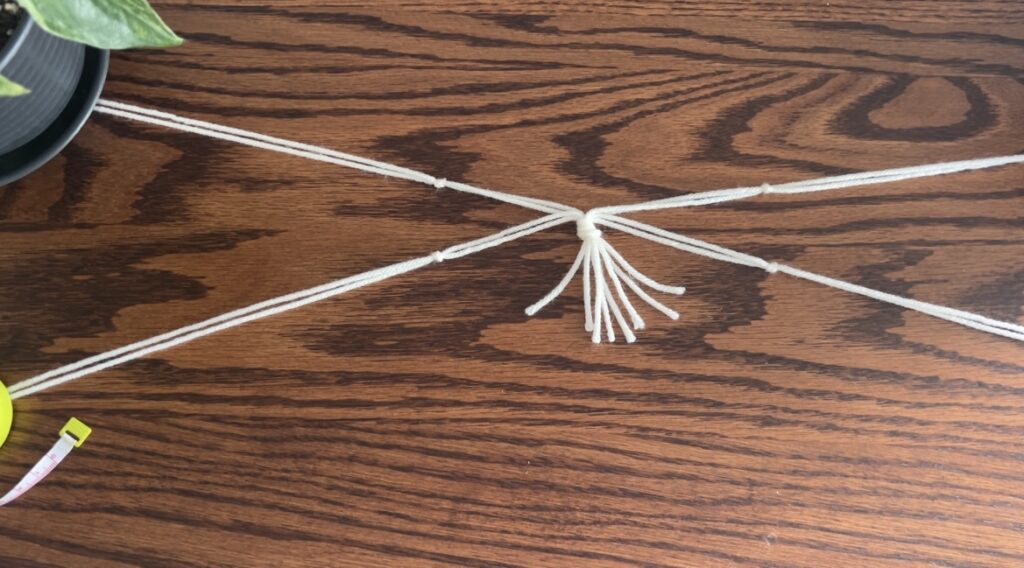 Four knots tied on white strings of yarn laying on wooden surface