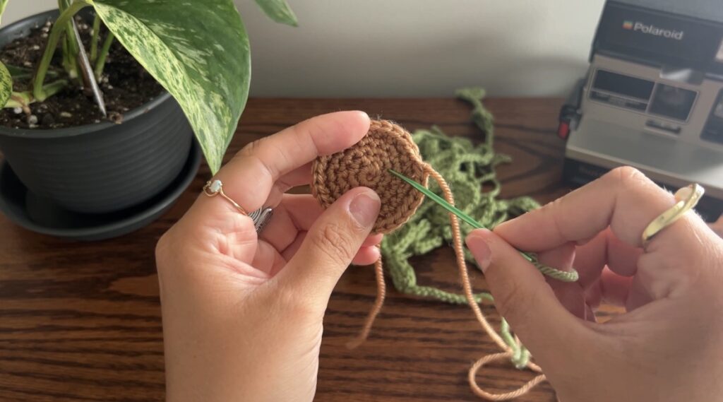Hand holding darning needle, attaching heart strings to brown crochet soil piece