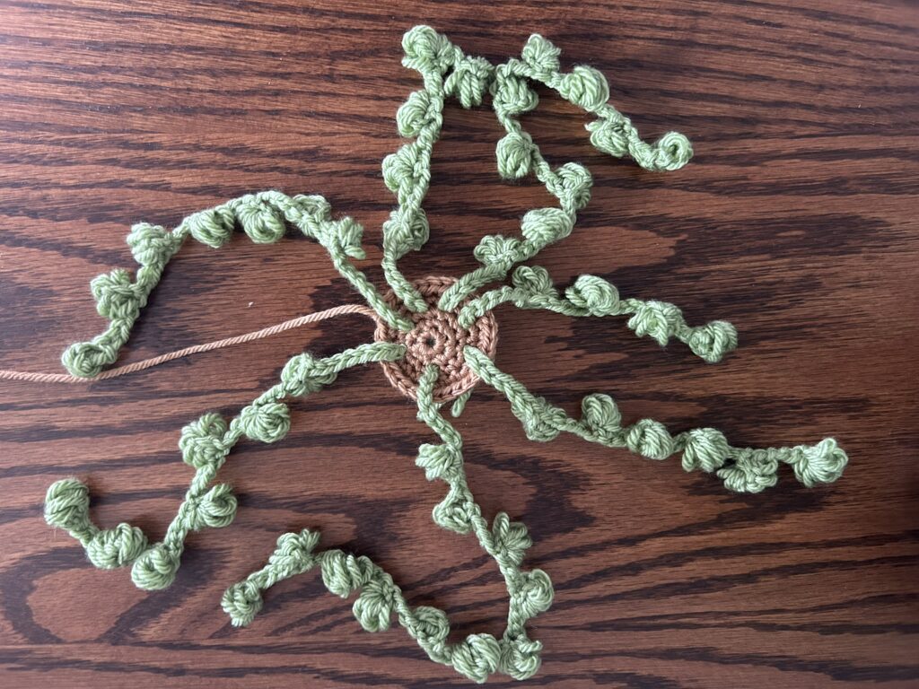green crochet bulb strings attached to light brown crochet soil laying on wooden surface top