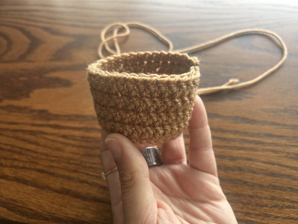 Hand Holding Brown Finished Crochet Pot above wooden surface