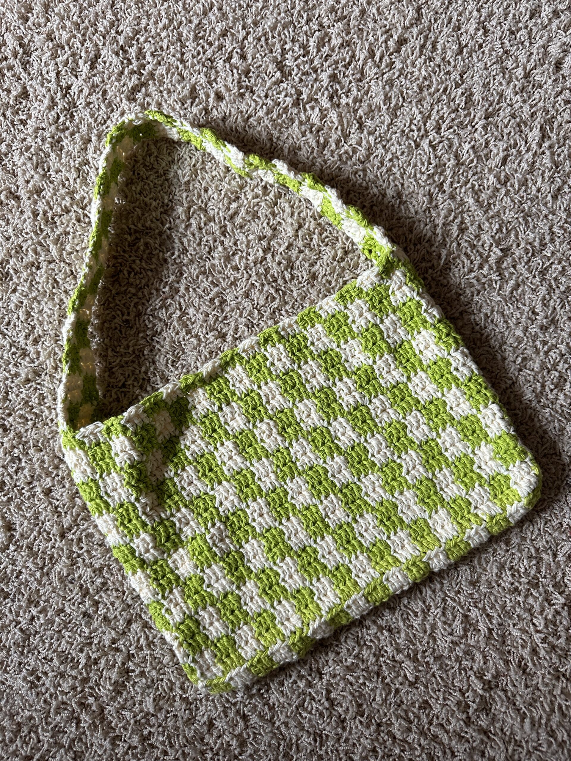 Handmade green and white checkered crochet tote bag laying on carpeted floor