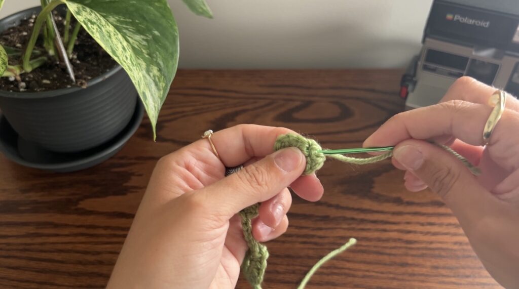 Hand holding green darning needle hiding end of string in green crochet vine piece