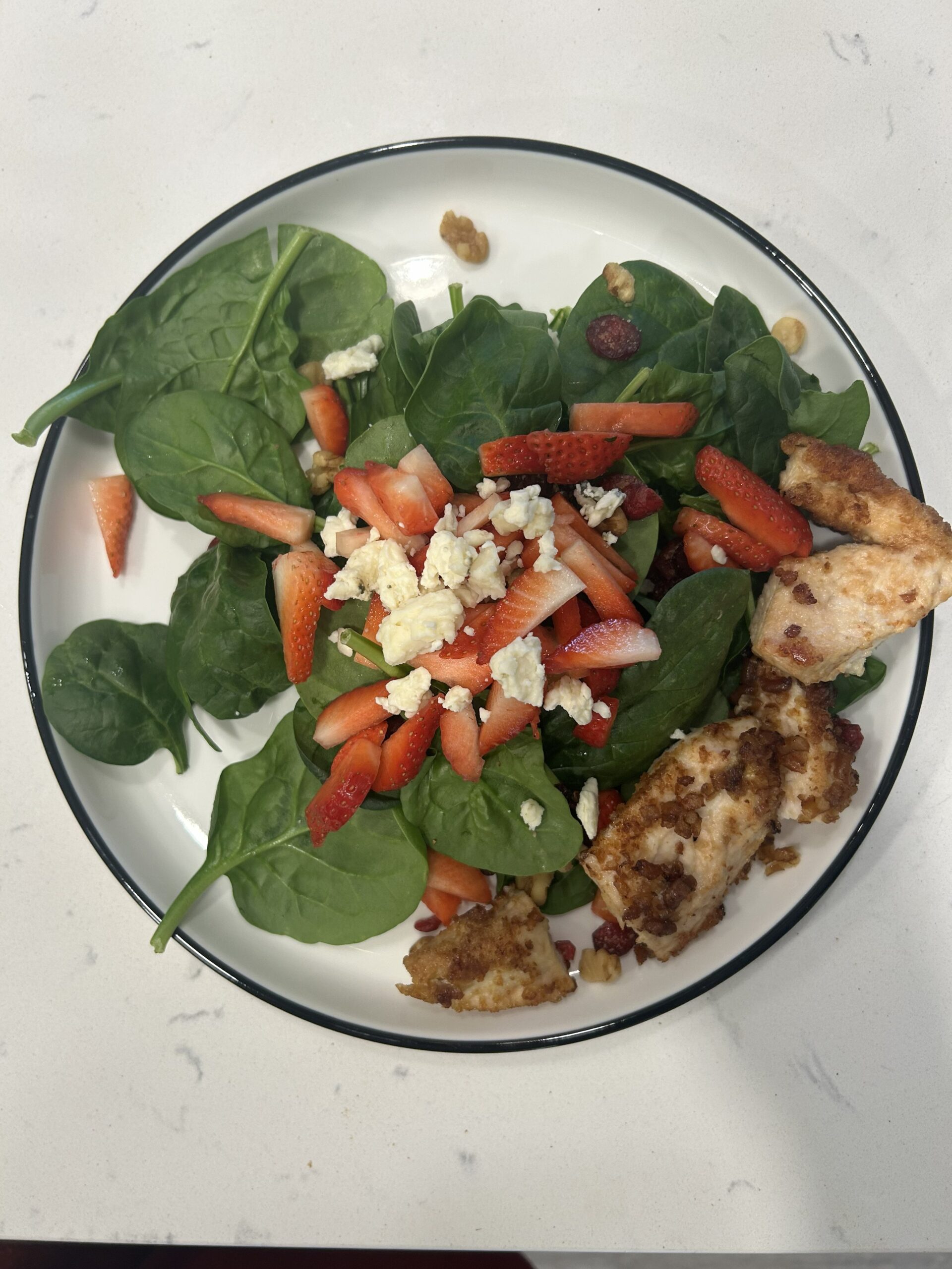 Spinach salad with strawberries, chicken and goat cheese on white plate and marble countertop