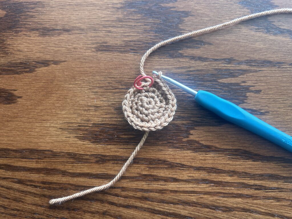 crochet hook and brown yarn showing round 4 of the crochet pattern laying on wooden surface