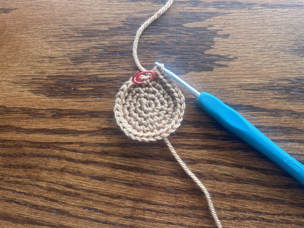 crochet hook and brown yarn laying on wooden surface showing round 5 of the crochet pattern