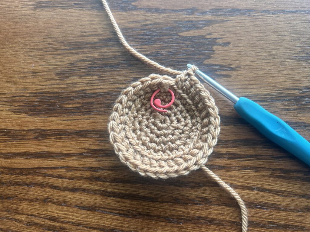 crochet hook, brown yarn and red stitch marker showing round 6 of the crochet pattern, laying on wooden surface