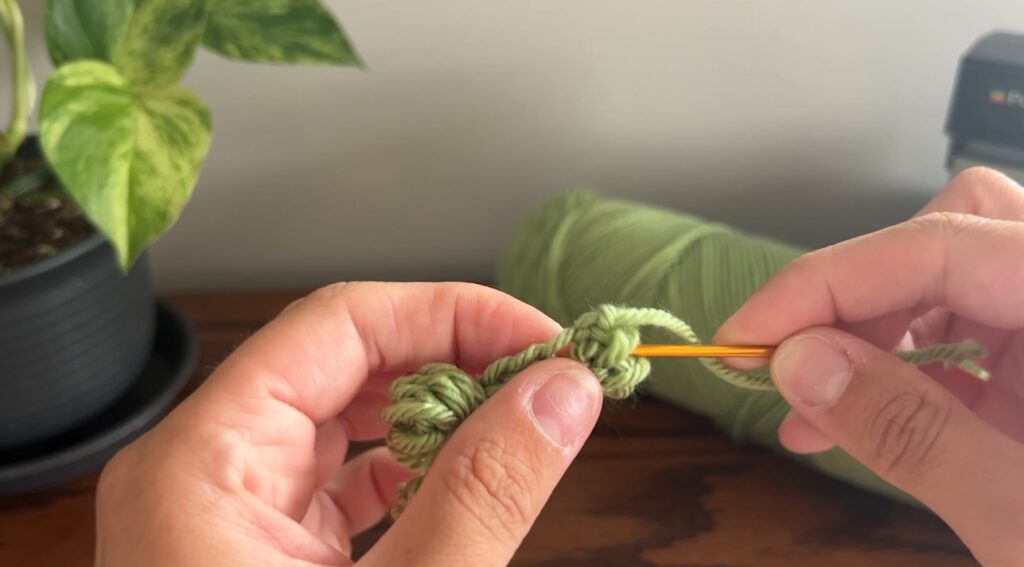 Hand holding darning needle and green crochet string weaving in the tail with the darning needle