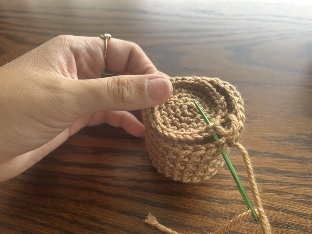 Green Darning needle placed between four stitches in a brown crochet pot forming a whip stitch